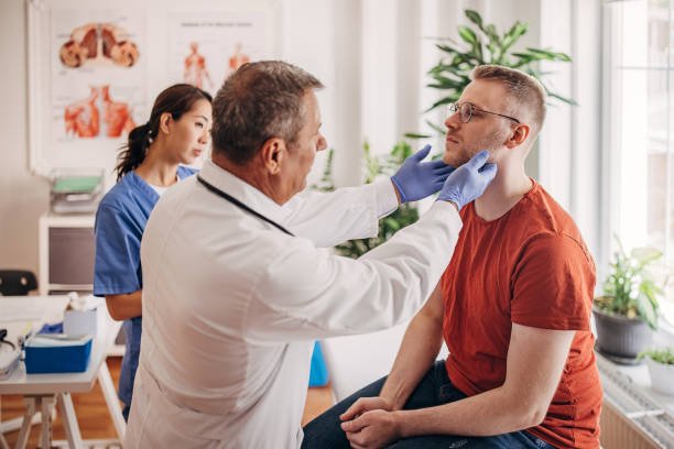 Doctor is examining the patient's glands at the clinic while nurse is taking notes in medical chart