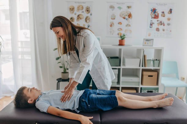 Female doctor is examining young boy' s stomach and intestines on the medicinal table