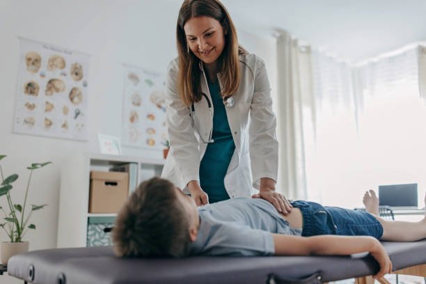 Female doctor is examining young boy' s stomach and intestines on the medicinal table